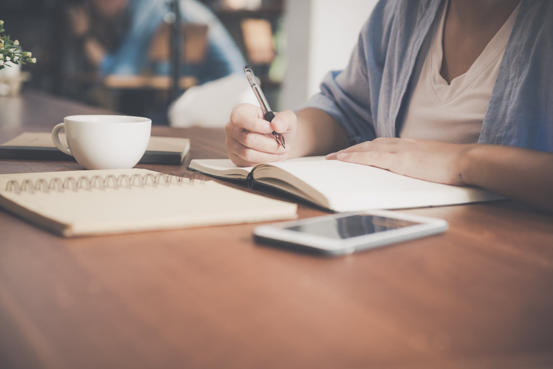 woman writing on a notebook beside teacup and tablet computer learning to write blogging as a doctor